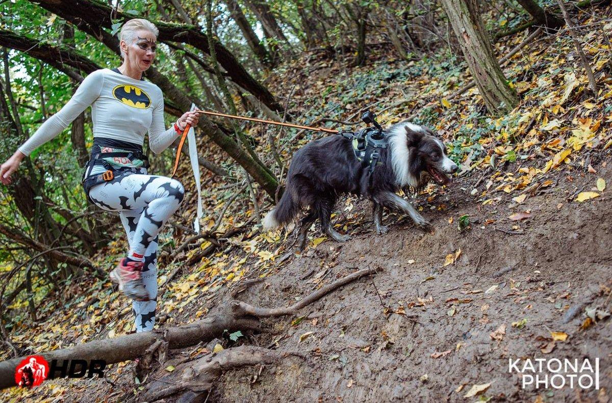 Batgirl jelmezes nő fut az erdőben kutyájával